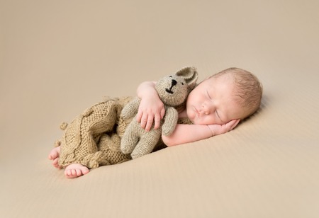 sweet sleeping newborn baby embracing toy-hare on blanketの写真素材