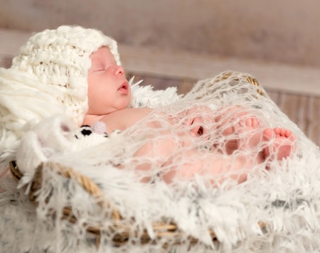 lovely face of newborn baby in knitted white hat lying on furの写真素材