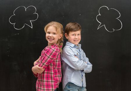 two little smiling children standing back to back with phrase clouds drawn on the blackboardの写真素材