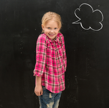 cute smiling little schoolgirl standing in front of the blackboard with drawn phrase cloud on itの写真素材