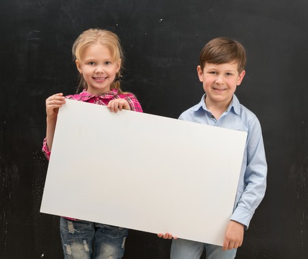 two cute smiling schoolchildren with blank sheet of paper in handsの写真素材