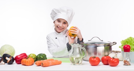 little girl-cook by table with vegetables in white uniformの写真素材