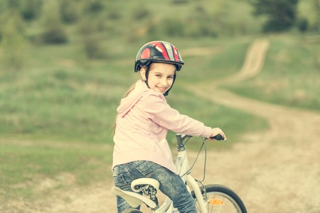 smiling little girl riding a bike in helmet turned awayの写真素材