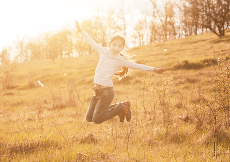 smiling little girl jumping on sunlight in countryside on a hillの写真素材