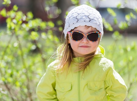 portrait of little smiling girl in sunglasses in a park in springの写真素材