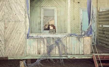 beautiful little girl standing on porch of abandoned wooden cabinの写真素材