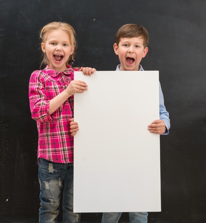 two cute smiling schoolchildren with blank sheet of paper in handsの写真素材