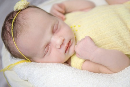 beautiful sleeping newborn girl in yellow costume anf flower on head, close-upの写真素材