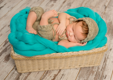 funny asleep newborn baby in wicker cot with knitted hat and pantsの写真素材