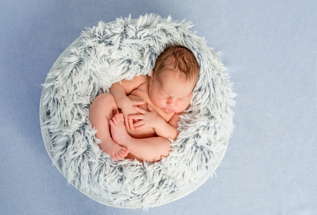 funny little naked newborn baby with crossed legs sleeping in basket, top viewの写真素材