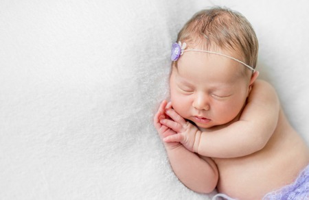 lovely newborn girl sleeping with hands under head with violet flower and panties, top viewの写真素材