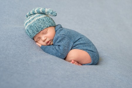 sleeping newborn baby in blue knitted jumpsuit and hat with crossed legsの写真素材