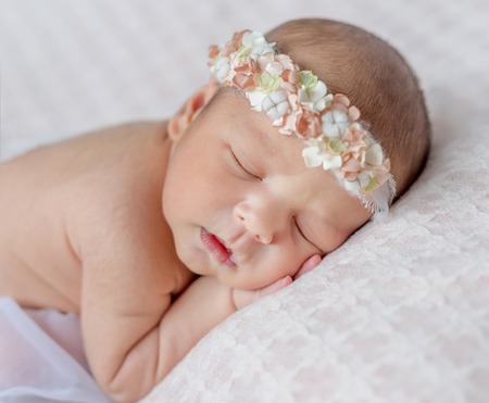 funny sleeping newborn girl with her hands under her head and headband with flowersの写真素材