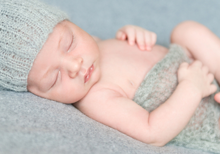 peacefully sleeping newborn baby in gray knitted hat covered with blanket, close-upの写真素材