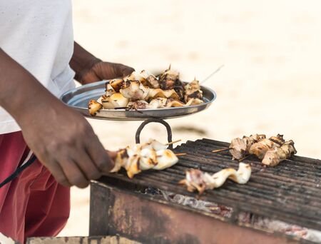 freshly barbecued seafood on grill and on plate in hands of a man