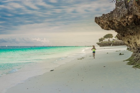 ZANZIBAR, TANZANIYA- JULY 17: tourist girl jogging on beautiful african beach with rockson on July 17, 2016 in Zanzibar, Tanzaniaのeditorial素材