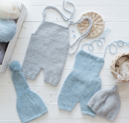Simple knitted handmade clothes for infant boys, pants and hats, blue and pastel gray, topviewの写真素材