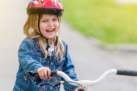 cute little girl in helmet and denim jacket on a bikeの写真素材