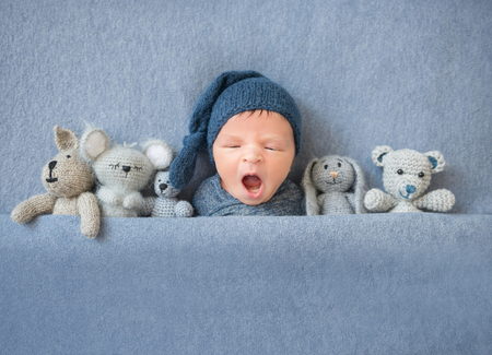 Newborn baby boy yawning and lying between plush toysの写真素材