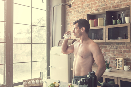 Athletic man drinks water with lemon in the kitchenの写真素材