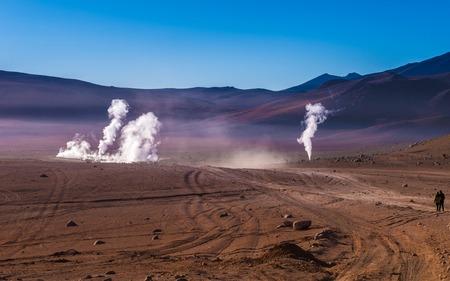 View of wide sunshine mountanious Bolivian desert and couple looking at the steaming geysersの写真素材