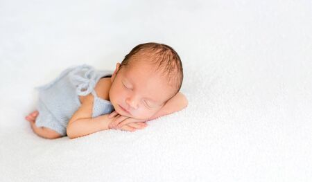 Newborn beatiful cute baby sleeping curled up in white blanket on white bed backgroundの写真素材