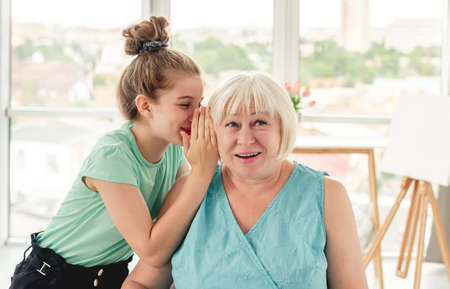 Little girl whispering secret to grandmotherの写真素材