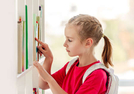 Schoolgirl searching book on library shelfの写真素材