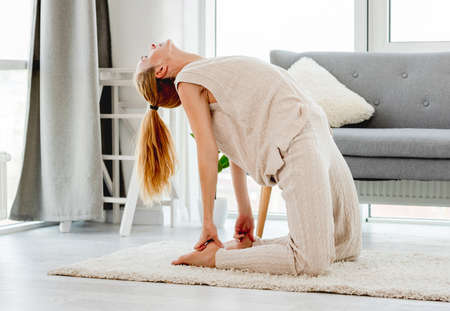 Beautiful young girl making yoga exercices for back flexibility in sunny room