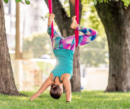 Girl during fly yoga practice in hammock stretching and relaxing her body at nature. Young woman doing aero fitness gymnastic exercising in the parkの写真素材