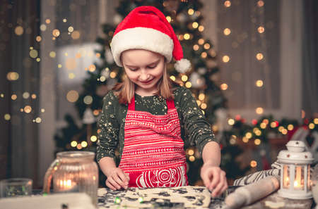 Little girl in santa hat cutting cookiesの写真素材