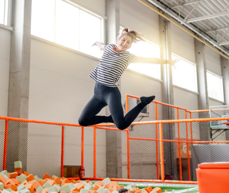 Pretty girl in trampoline park jumping with split and smiling. Happy teenager enjoying amusement activitiesの写真素材