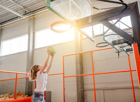 Pretty child girl in trampoline park put ball in basketball basket. Happy preteen kid enjoying amusement activities and sportの写真素材