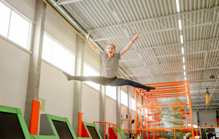 Pretty girl in trampoline park jumping and making split pose in air. Happy teenager enjoying amusement activities and stretchingの写真素材