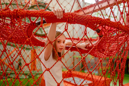 Pretty child girl in net in amusement park having fun. Happy preteen kid enjoying entertainment activitiesの写真素材