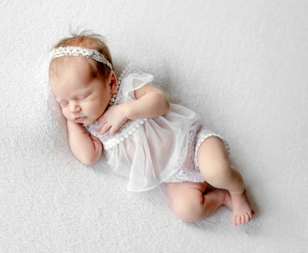 Newborn baby girl wearing wreath and tender dress sleeping holding tiny hands under her cheek. Infant child kid napping studio portraitの写真素材
