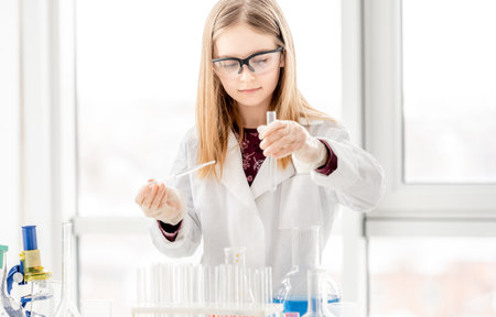 Smart girl during scientific chemistry experiment wearing protection glasses, holding tubes and measuring ingridients. Schoolgirl with chemical equipment on school lessonの写真素材