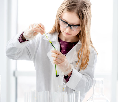 Smart girl during scientific chemistry experiment wearing protection glasses, holding tubes and measuring ingridients. Schoolgirl with chemical equipment on school lessonの写真素材