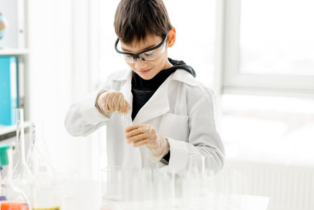 School boy wearing protection glasses doing chemistry experiment in elementary science class. Pupil with equipment tubes in labの写真素材