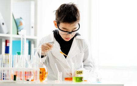 School boy wearing protection glasses with dirty face doing chemistry experiment in elementary science class. Clever pupil in labの写真素材
