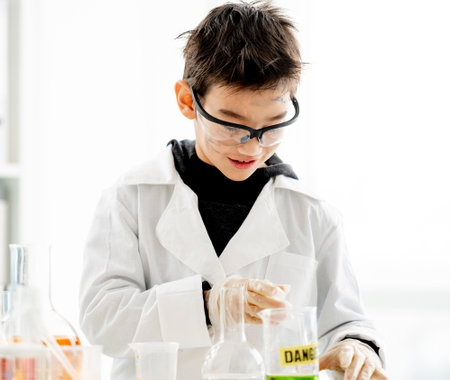 School boy wearing protection glasses with dirty face doing chemistry experiment with chemical liquids in elementary science class. Clever pupil analyzing results of test in labの写真素材