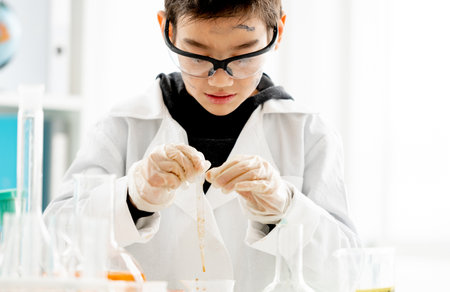 School boy wearing protection glasses with dirty face doing chemistry experiment with chemical liquids in elementary science class. Clever pupil analyzing results of test in labの写真素材