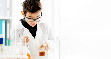 School boy wearing protection glasses doing chemistry experiment in elementary science class and mix components. Clever pupil with dirty face in lab during testの写真素材