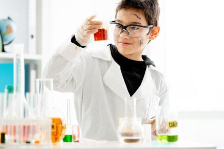 School boy with dirty face wearing protection glasses looking at liquid in glass during chemistry experiment in elementary science class and smiling. Clever pupil in lab during testの写真素材