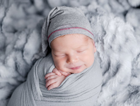 Cute newborn baby boy swaddled in grey fabric sleeping on fur blanket. Adorable infant child kid napping studio portraitの写真素材