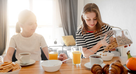 Girls sisters eat tasty breakfast together and filling plate with oat cereal meal. Female child kid and subling with musli food during morning nutritionの写真素材