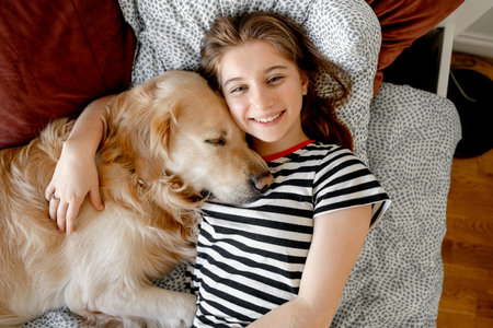 Pretty girl hugging golden retriever dog and lying in bed. Female teenager with purebred doggy pet labrador resting togetherの写真素材