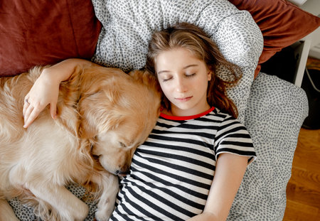 Pretty girl hugging golden retriever dog and sleeping in bed. Female teenager with purebred doggy pet labrador resting napping togetherの写真素材