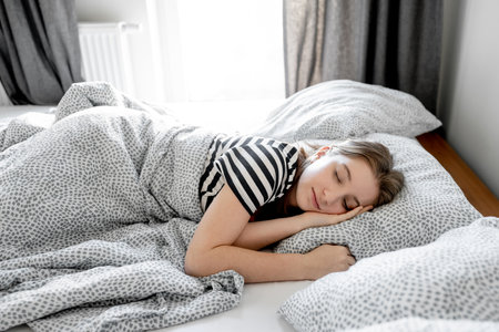 Pretty girl teenager sleeping in bed in morning with sun light. Young female person napping at homeの写真素材