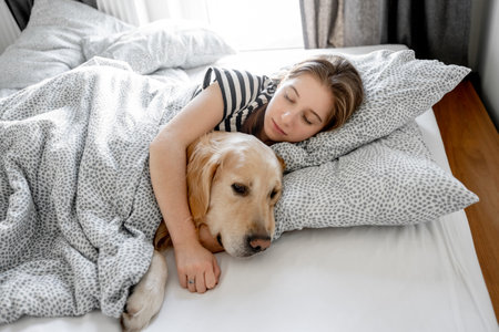 Pretty girl hugging golden retriever dog and sleeping in bed. Female teenager with purebred doggy pet labrador resting napping togetherの写真素材